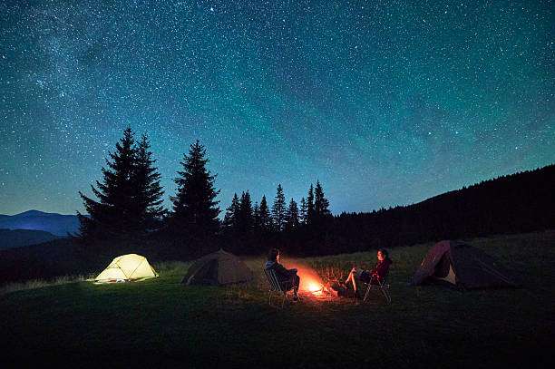 Camping under starry sky, campfire, and glowing tent, no headlamp visible.