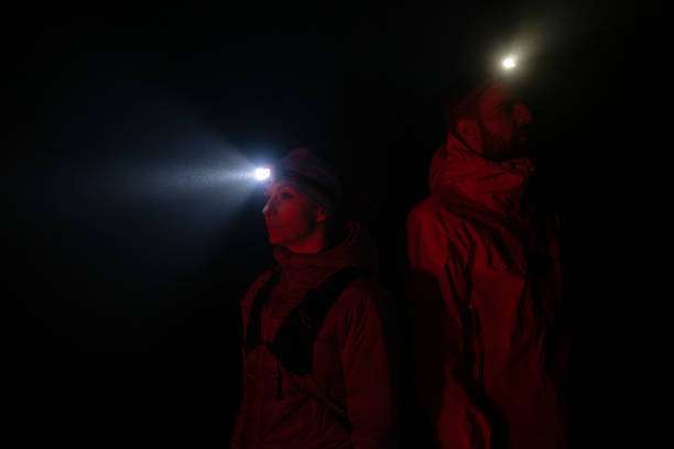 Two people with red headlamp beams illuminating the dark
