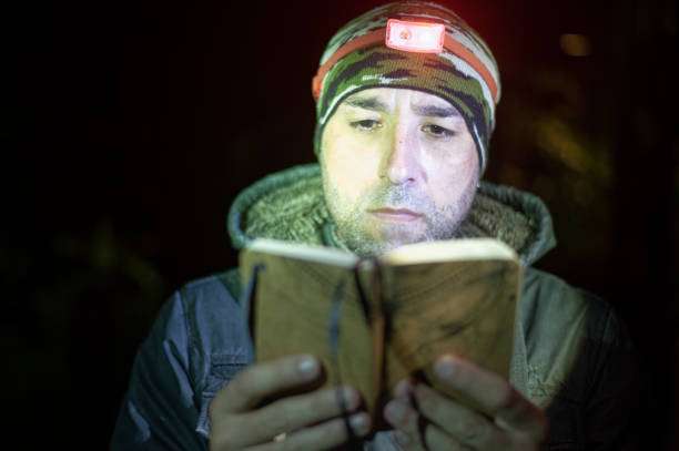 Man reading book at night with headlamp.