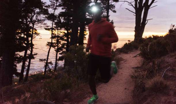 Man trail running at sunrise, wearing a bright headlamp for visibility. Ideal for adventurers.