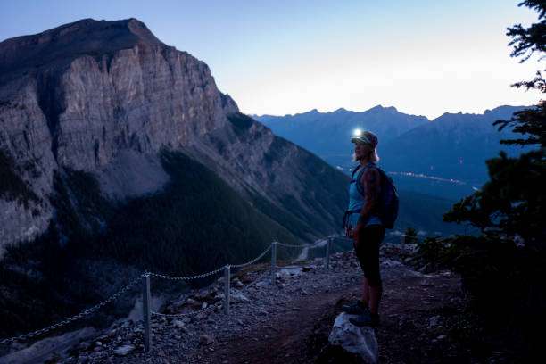 Woman with headlamp on mountain trail at dusk.