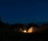 Camping tent illuminated by campfire and headlamp light at night.