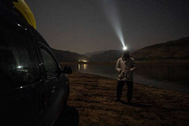 Man wearing headlamp shines light by lake at night