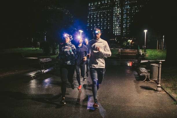 Group of runners wearing bright headlamps illuminate a city park path at night.