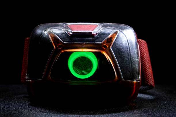 Close-up of a glowing green headlamp on a dark surface, ready for use.