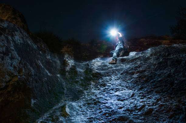 Person climbing rocky terrain at night, illuminated by a bright headlamp.