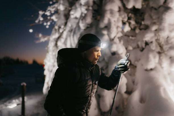 Person wearing headlamp checks gear in snowy forest at dusk.