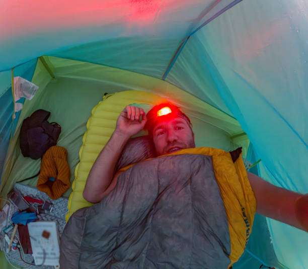 Man in tent wearing red headlamp while sleeping bag.