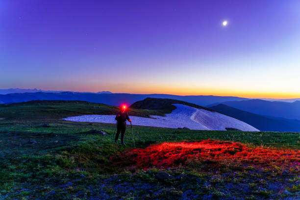 Hiker wearing a headlamp in mountains at twilight.