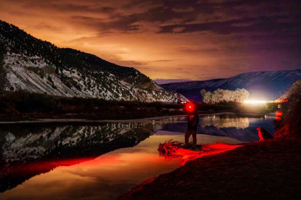 Person with red headlamp at riverbank during sunset