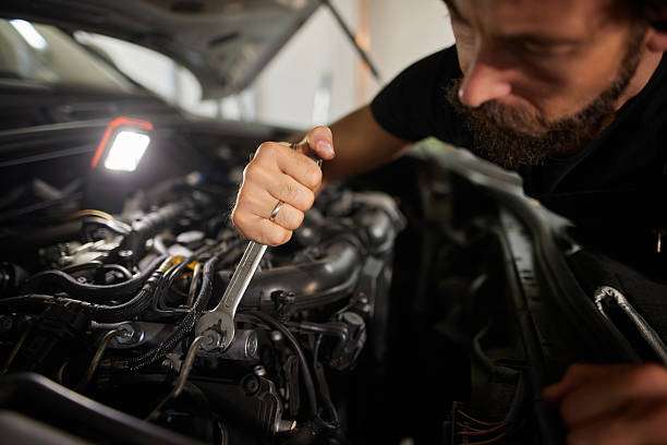 Mechanic working on car engine, needing a powerful headlamp for detailed repairs.