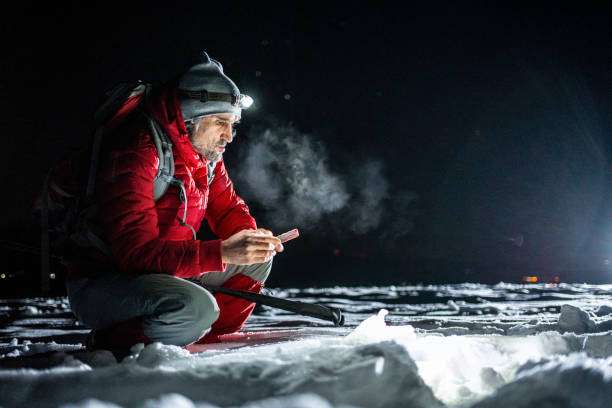 Man with headlamp uses phone in snowy landscape at night.