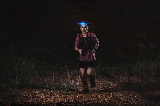 Runner with bright blue headlamp on night trail.