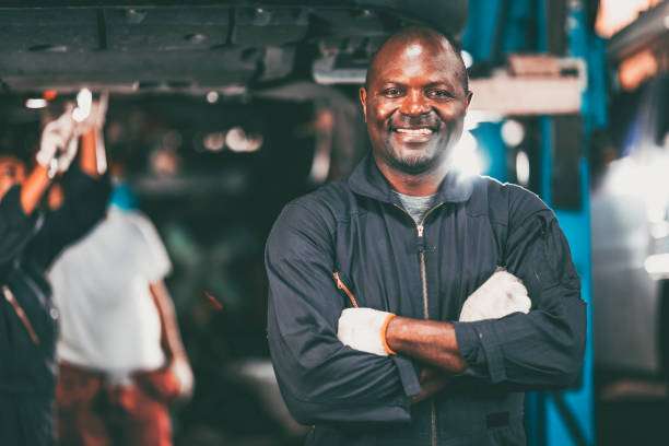 Smiling mechanic in a garage, ready for work, even tasks requiring a good headlamp.